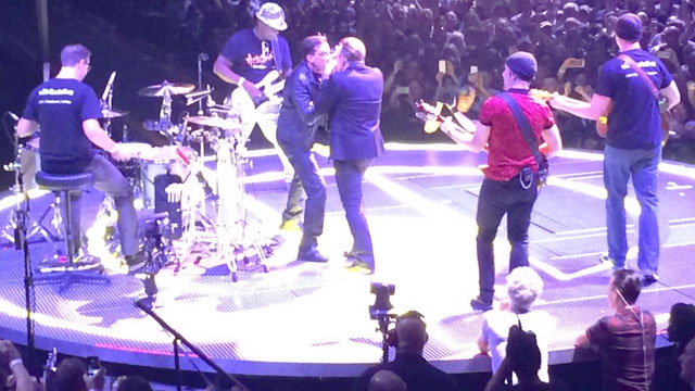 Bono e The Edge acompanham banda cover canadense. Enquanto isso, Larry e Adam assistem no pé do palco